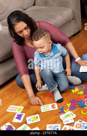 ragazzo di 3 anni con sua madre, giocando con carte numeriche che hanno un pezzo di puzzle che si inserisce all'interno della carta, contando e indicando l'apprendimento a casa Foto Stock