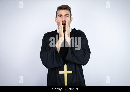 Giovane uomo ispanico che indossa uniforme sacerdote in piedi su sfondo bianco scioccato bocca di copertura con le mani per errore. Concetto segreto. Foto Stock