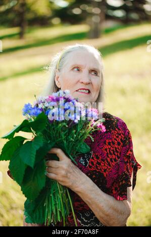 80 anno vecchia donna con un mazzo di fiori nelle sue mani. Foto Stock