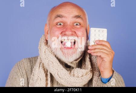 Uomo malato in sciarpa con pillole da mal di gola. Pillola di trattamento. Medicina. Uomo anziano che prende le pillole farmaceutiche Foto Stock