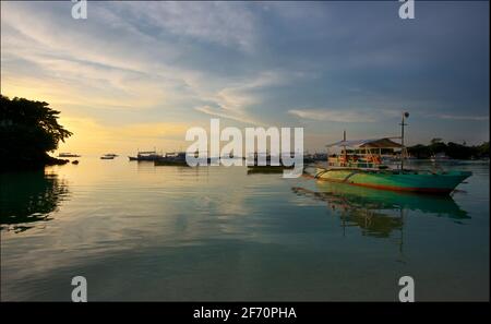 Barca con gli Outrigger ormeggiati al largo di Logon, Malapascua Island al tramonto. Mare di Visayan, Cebu, Filippine. Foto Stock