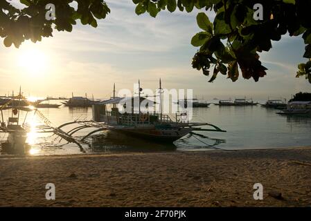 La spiaggia sabbiosa di Logon, isola di Malapascua, con le canoe Outrigger sulla spiaggia al tramonto. Mare di Visayan, Cebu, Filippine. Foto Stock