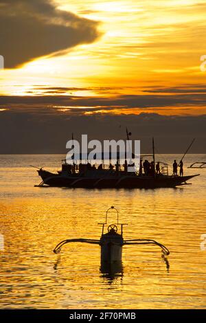 Barche ormeggiate nella baia al largo del villaggio di Logon, Malapascua Island. Mare di Visayan, Cebu, Filippine. Sagome di barche al tramonto. Foto Stock