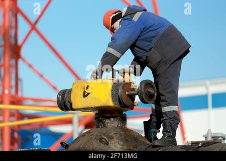 Un lavoratore in tute e un elmetto ripara e mantiene una gru lineare del gasdotto principale sulla strada in inverno. Foto Stock