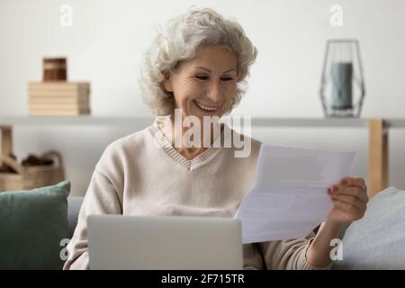 Donna anziana felice con il laptop che legge la lettera di carta a casa Foto Stock