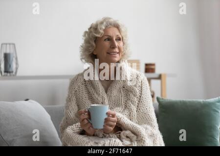 Felice donna anziana pensiva anni '60 avvolta in plaid di lana Foto Stock