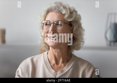 Felice anziana signora pensiva indossare occhiali, guardando la finestra Foto Stock
