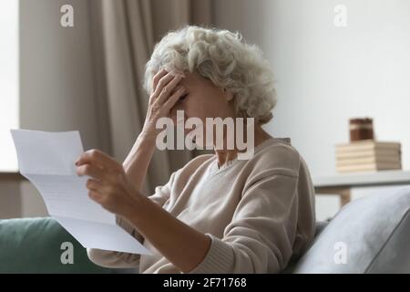 Donna anziana sconvolta seduta sul divano a casa Foto Stock