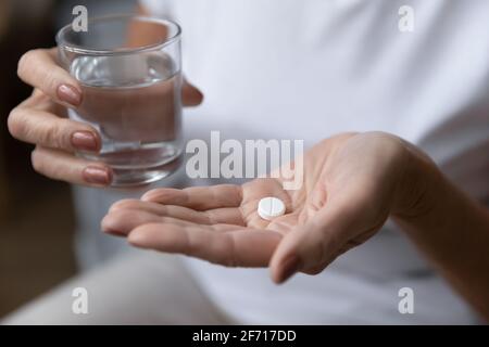 Donna matura che tiene un bicchiere d'acqua e prende painkiller Foto Stock
