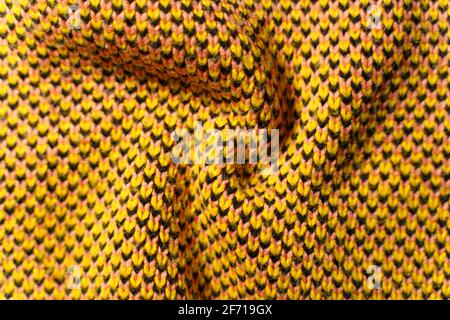 Pieghe ritorte di tessuto sintetico a maglia con elementi di disegno di filati gialli, neri e bianchi da vicino. Tessuto lavorato a maglia multicolore Foto Stock