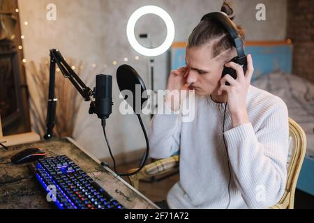 Bel ragazzo sta registrando podcast utilizzando il microfono e creando contenuti per blog audio. Uomo indossò le cuffie e iniziò a lavorare a casa. Suono Foto Stock