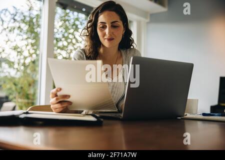 Donna che legge un documento mentre lavora su un computer portatile. Donna che lavora da casa. Foto Stock