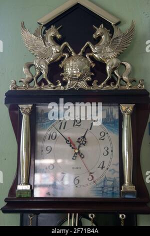 Vecchio orologio a pendolo in legno con decorazione – cavalli con ali e altri dettagli appesi su un muro, orologio da parete vintage, oggetto Foto Stock