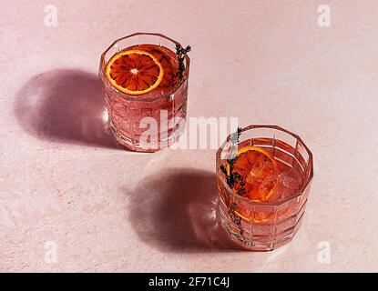 Cocktail di gin rosa con arancio di sangue rosso e ghiaccio in giornata di sole. Riflessi duri alla moda. Foto Stock