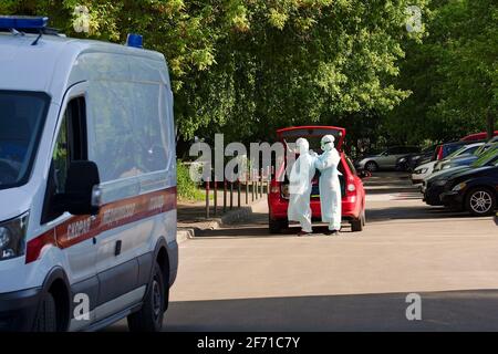Mosca, Russia - 7 giugno 2020. COVID-19. I medici indossano un costume protettivo prima di visitare un paziente. Sulla macchina c'è un'iscrizione in russo per a. Foto Stock