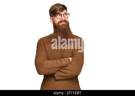 Giovane irlandese rosso uomo che indossa abiti casual e occhiali cercando al fianco con le braccia incrociate convinte e fiduciose Foto Stock