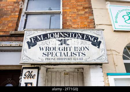 Segno di nome dipinto di F M Johnston, Eng, spcialisti di ferro battuto, sopra una porta in South Street, Bridport, una città di mercato in Dorset, Inghilterra sud-occidentale Foto Stock