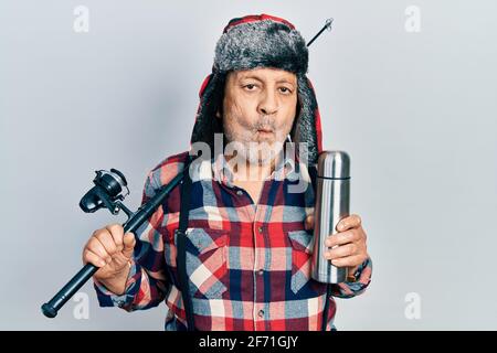 Bell'uomo maturo che indossa attrezzatura di pescatore e termo facendo faccia di pesce con bocca e occhi squinting, pazzo e comico. Foto Stock