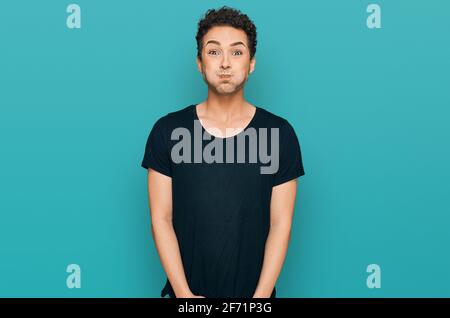 Giovane bell'uomo che indossa casual t shirt nera soffia le guance con il viso divertente. Bocca gonfia con aria, espressione pazza. Foto Stock