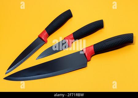 Impostare i coltelli da cucina con un manico nero su sfondo giallo. Foto Stock