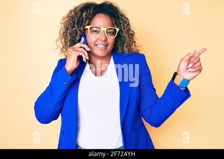 Giovane afroamericano più taglia donna che indossa occhiali che hanno conversazione parlare sullo smartphone sorridendo felice indicando con la mano e. dito a ° Foto Stock