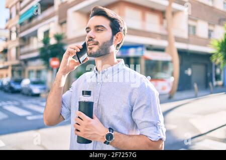 Giovane ispanico che tiene una bottiglia d'acqua e parla con lo smartphone in città. Foto Stock