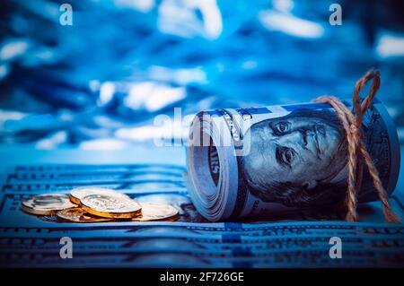 Pile di monete e un rotolo di dollari contro uno sfondo di centinaia di dollari fatture sono sparsi in tutto lo spazio. Le monete sono lucide, dorate dentro Foto Stock