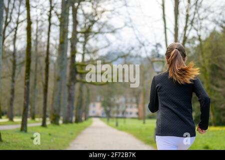 Primo piano vista posteriore di una donna in forma che fa jogging attraverso un parco boscoso in primavera in un concetto di a. sano stile di vita attivo all'aperto Foto Stock