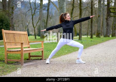 Donna sportiva che si adopera facendo esercizi di stretching per tonificare e rinforzare i muscoli all'aperto in un parco in primavera in uno stile di vita sano all'aperto Foto Stock