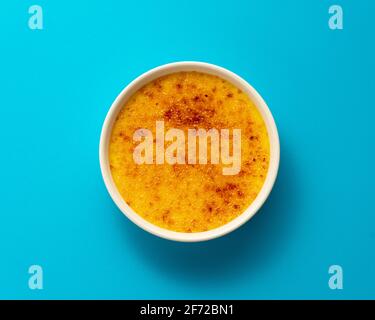 Creme brulee in ramekin isolato su sfondo di colore blu brillante. Primo piano dessert francese. Crema bruciata. Crema spagnola catalana. Vista dall'alto Foto Stock