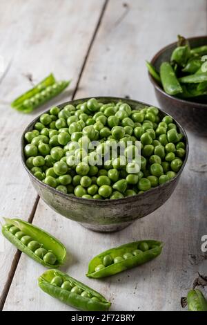 Piselli verdi freschi. Baccelli di piselli verdi freschi e piselli verdi in ciotola su sfondo di legno. Foto Stock