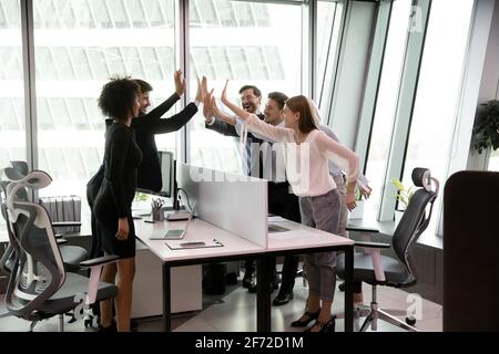 I dipendenti multirazziali entusiasti danno cinque in alto durante la riunione Foto Stock