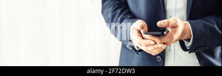 Uomo d'affari in tuta blu con uno smartphone nero in mano e chiacchierando con i colleghi. Foto Stock