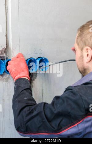 L'elettricista inserisce la scatola di plastica direttamente nei fori di uscita. Primo piano Foto Stock