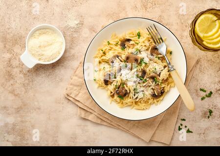 Pranzo risoni di pasta italiana, funghi, salsa, parmigiano, timo, aglio, olio d'oliva, in piastra bianca su ardesia, pietra o fondo di cemento. Vista dall'alto w Foto Stock