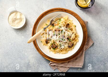 Pranzo risoni di pasta italiana, funghi, salsa, parmigiano, timo, aglio, olio d'oliva, in piastra bianca su ardesia, pietra o fondo di cemento. Vista dall'alto w Foto Stock