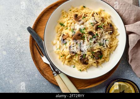 Pranzo risoni di pasta italiana, funghi, salsa, parmigiano, timo, aglio, olio d'oliva, in piastra bianca su ardesia, pietra o fondo di cemento. Vista dall'alto w Foto Stock