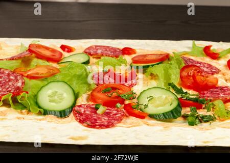 gli ingredienti per lo shawarma sono disposti su un pita sottile: pomodori, verdi, salumi, formaggi, cetrioli e lattuga da vicino Foto Stock