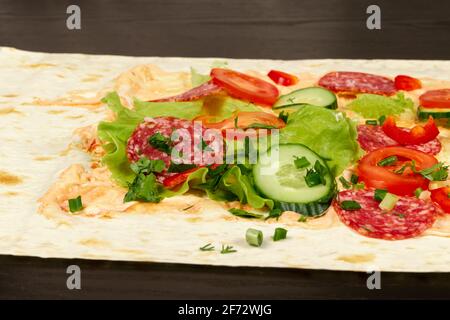 gli ingredienti per lo shawarma sono disposti su un pita sottile: pomodori, verdi, salumi, formaggi, cetrioli e lattuga da vicino Foto Stock