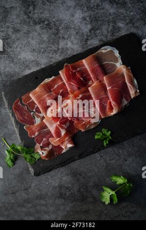 Prosciutto fresco affettato posizionato sulla vista dall'alto dell'ardesia Foto Stock