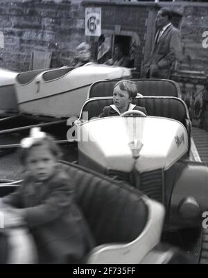 1956, bambini storici e giovani seduti in auto a bordo di un divertente o divertente giro in fiera, Bridlington, East Yorkshire, Inghilterra, Regno Unito. Un uomo è in piedi sopra la corsa e un segno per 6d può essere visto. La corsa qui vista è conosciuta come una corsa piatta in cui coloro che prendono parte sono su un piano parallelo al terreno che ruota intorno ad un asse verticale. Foto Stock