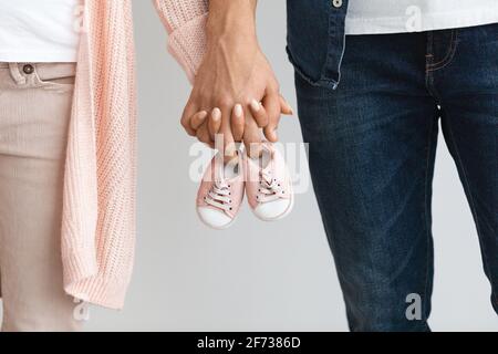 Primo piano di una coppia incinta che trasporta scarpe piccole per bambini mentre si tiene in mano mani insieme Foto Stock