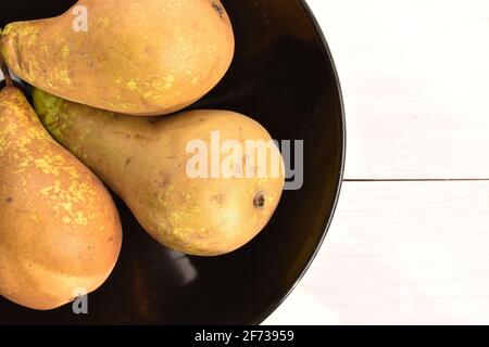 Tre pere da conferenza, biologiche, dolci, gustose, mature, primo piano, in una piastra di ceramica nera sullo sfondo di un tavolo in legno naturale, verniciato bianco. Foto Stock