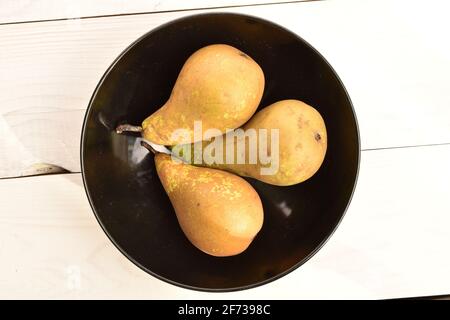 Tre pere da conferenza, biologiche, dolci, gustose, mature, primo piano, in una piastra di ceramica nera sullo sfondo di un tavolo in legno naturale, verniciato bianco. Foto Stock