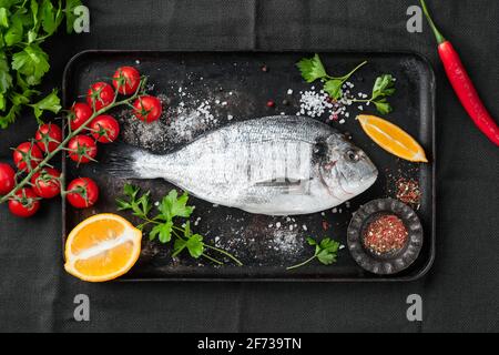 Pesce dorado crudo, spezie e verdure per cucinare su un vecchio vassoio di cottura in metallo nero, vista dall'alto Foto Stock