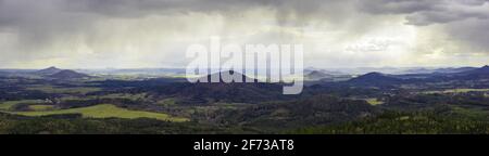 Vista panoramica sulle colline ondulate delle montagne Lusaziane bohemien con macchie di luce solare, nubi tempeste e piume piovose. Monte Ralsko, Monte Tlustek Foto Stock