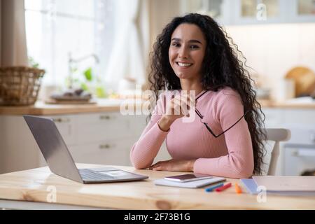Carriera freelance. Sorridente giovane donna seduto al tavolo con il computer in cucina Foto Stock