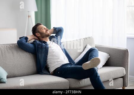 Felice uomo bearded che si rilassa sul divano a casa Foto Stock