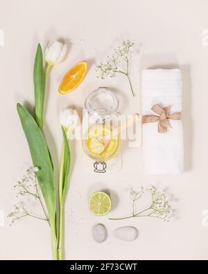 Eco-friendly, benessere, composizione termale con asciugamano, scrub agli agrumi, arancio, laim, accessori da bagno naturali e fiori su sfondo chiaro. Pelle domestica Foto Stock