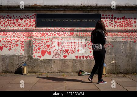 Londra, Regno Unito. 4 aprile 2021. Una donna vede i cuori la domenica di Pasqua su un muro a Lambeth, vicino al Tamigi, con ogni cuore che rappresenta qualcuno che è morto durante la pandemia di coronavirus in corso nel Regno Unito. Chiamato il National Covid Memorial Wall, è stato creato dal gruppo chiamato Covid-19 famiglie in lutto per la giustizia con il lavoro che inizia una settimana fa e si estende per mezzo miglio per il momento in cui è completo. Credit: Stephen Chung / Alamy Live News Foto Stock